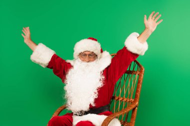 Heyecanlı Noel Baba yeşil üzerinde izole bir şekilde sallanan sandalyede oturuyor.