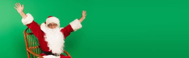Heyecanlı Noel Baba hasır sandalyede yeşil pankartta tek başına oturuyor. 