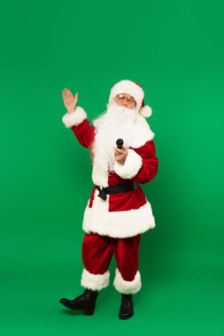 Noel Baba 'nın elinde mikrofon ve yeşil arka planı var.