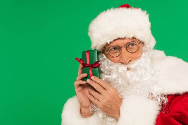 Gözlüklü Noel Baba yeşilde izole edilmiş kurdeleli hediye kutusu taşıyor.
