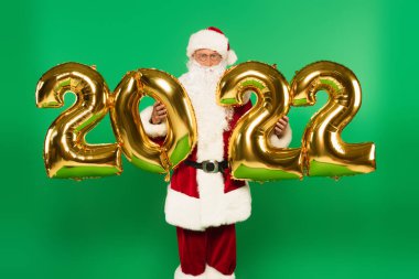 2022 şeklinde balonları tutan, yeşil üzerine izole edilmiş Noel Baba.