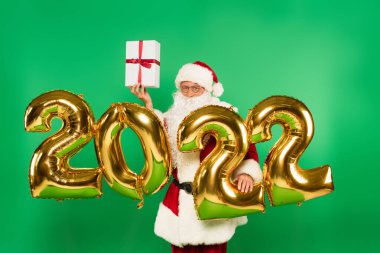 Noel Baba 2022 numaralı balonların yanında hediye tutuyor yeşil üzerinde izole edilmiş numaralar.