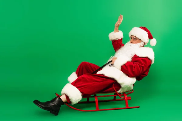 Santa Claus Mává Rukou Zatímco Sedí Saních Zeleném Pozadí — Stock fotografie