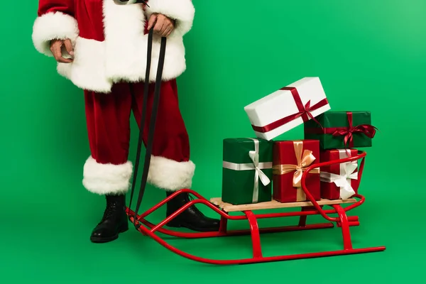 用绿色背景的雪橇站在礼物旁边的桑塔爪的剪影 — 图库照片