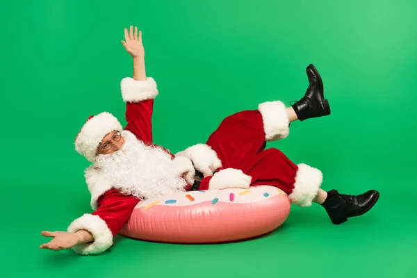圣诞老人用手指指着 躺在绿色背景的泳圈上 — 图库照片