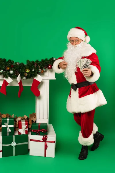 Santa Claus Ukazuje Dolary Blízkosti Krbu Dárky Zeleném Pozadí — Stock fotografie