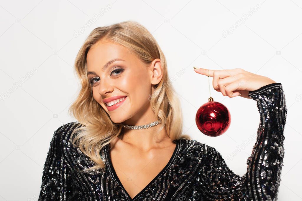 smiling blonde woman in shiny necklace and blouse with sequins holding christmas ball isolated on white