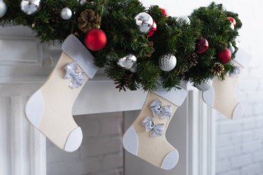 Takılar ve Noel çoraplarıyla süslenmiş yeşil çam çelenkli şömine.