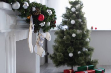 Süslü çelenk ve yılbaşı çoraplarıyla süslenmiş şömine, bulanık Noel ağacının yanında.
