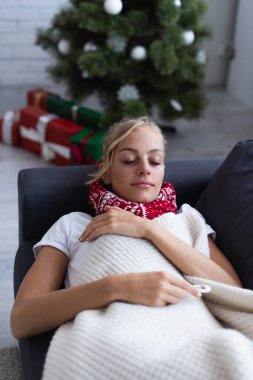 Hasta kadın hediyelerin yanında kanepede uyuyor ve bulanık arka planda noel ağacı var.
