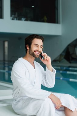 Kaplıcadaki bulanık yüzme havuzunun yakınında akıllı telefondan konuşan neşeli bir adam. 