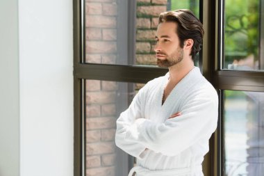 Bornozlu adam spa merkezinde pencerenin yanında duruyor. 