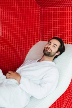 Bornozlu genç adam spa merkezindeki şezlongda dinleniyor. 