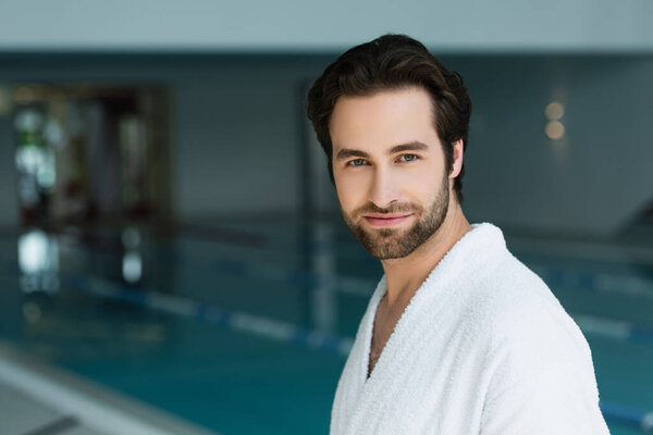 Young man in white bathrobe looking at camera in spa center 