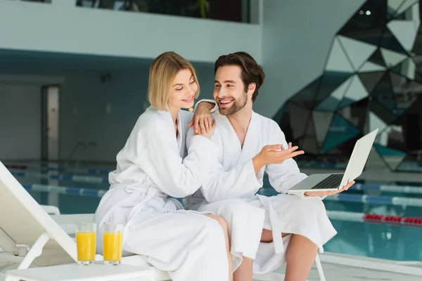 Hombre Sonriente Apuntando Computadora Portátil Cerca Novia Albornoz Jugo Naranja — Foto de Stock