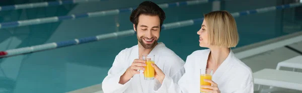 Alegre Pareja Batas Blancas Sosteniendo Vasos Jugo Naranja Centro Spa — Foto de Stock