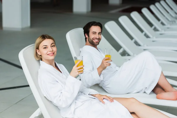 Ung Kvinna Som Håller Apelsinjuice Nära Suddig Pojkvän Solstol Spa — Stockfoto