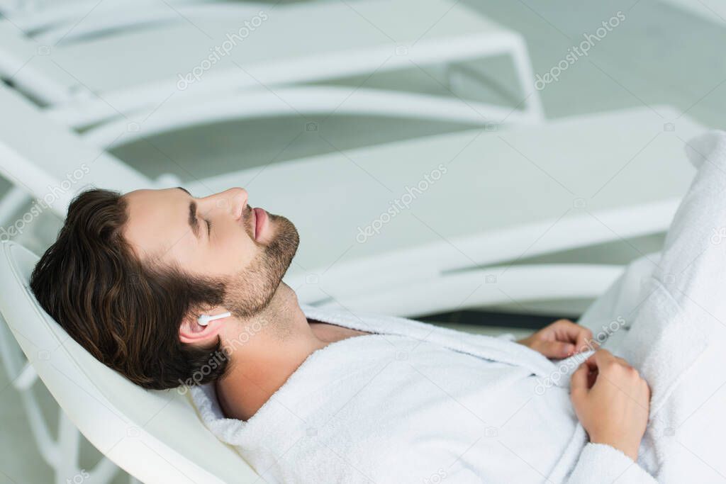 Man in wireless earphone relaxing on deck chair in spa center 