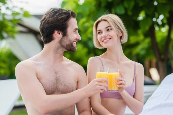 笑顔男クリンクオレンジジュースとともにガールフレンドで水着オンリゾート — ストック写真