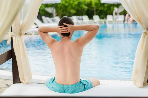 Bakåt Syn Man Badbyxor Sitter Loungen Säng Nära Poolen Resort — Stockfoto