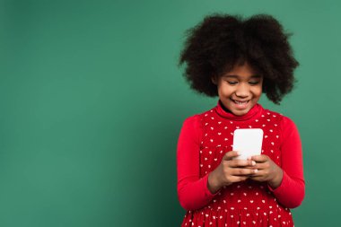 Kırmızı elbiseli, gülümseyen Afrikalı Amerikalı kız yeşil arka planda cep telefonu kullanıyor. 