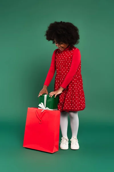 Sonriente Chica Afroamericana Vestido Poner Presente Bolso Compras Rojo Sobre —  Fotos de Stock