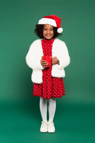 African American Child Santa Hat Fluffy Jacket Holding Cup Green — Stock Photo, Image