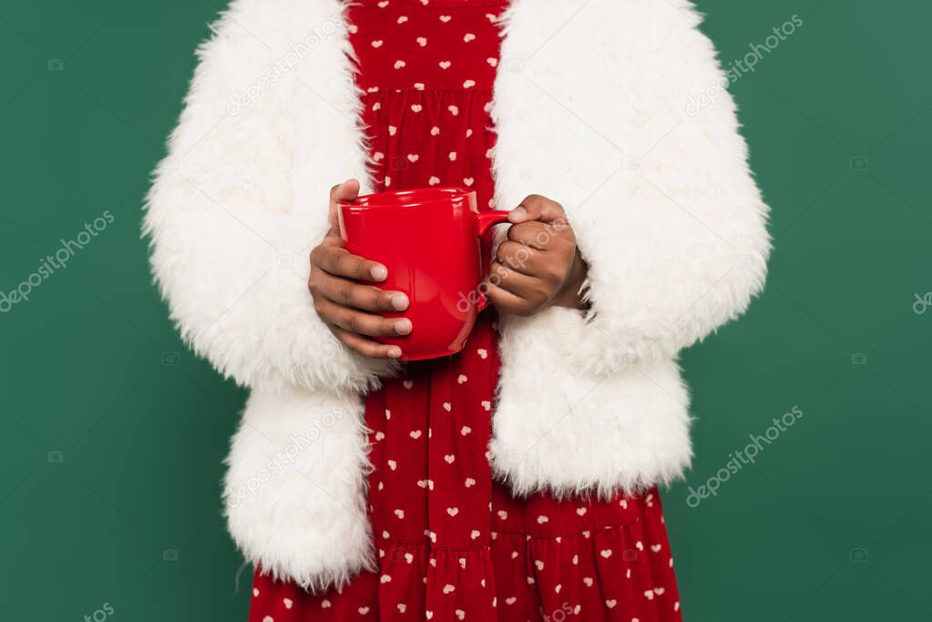 Cropped view of african american girl in fluffy jacket holding cup isolated on green 