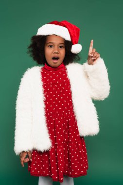 Heyecanlı, tüylü ceketli ve Noel Baba şapkalı Afro-Amerikan kızı. 