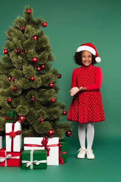 Smiling African American Girl Santa Hat Pointing Presents Christmas Tree — Stock Photo, Image