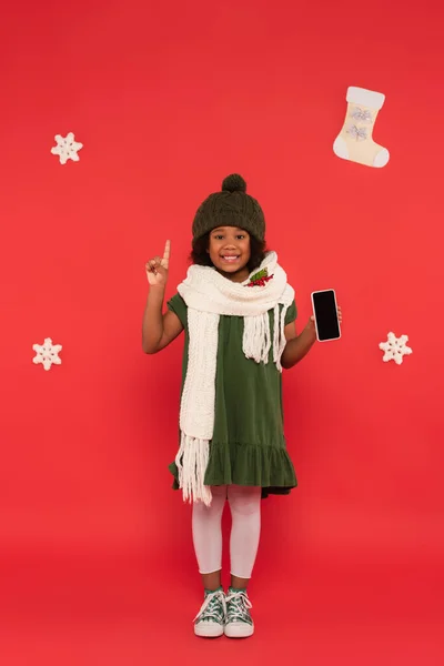 Uśmiechnięty Afrykański Dzieciak Szaliku Jemiołą Trzymający Smartfona Mający Pomysł Pobliżu — Zdjęcie stockowe