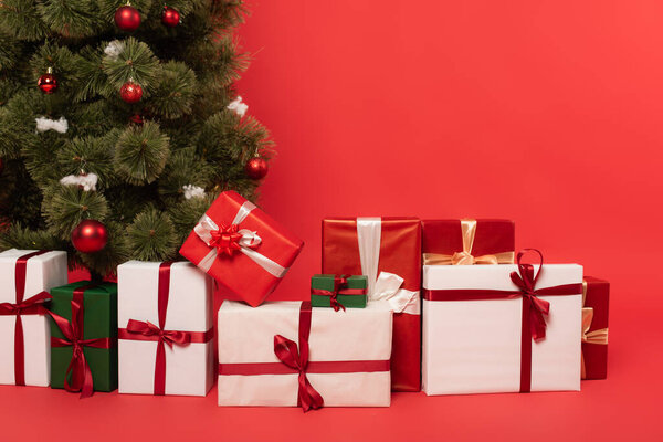 Presents near decorated christmas tree on red background