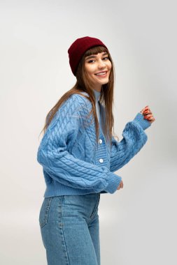 Şık bir genç kadın sıcak bir süveter ve şapka giyer, neşeli duruşuyla ve sıcaklığıyla..