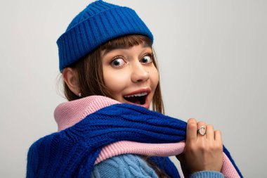 Genç bir kadın, keyifle poz verirken rahat bir eşarp ve parlak bir şapka takarak mevsimin tadını çıkarıyor..