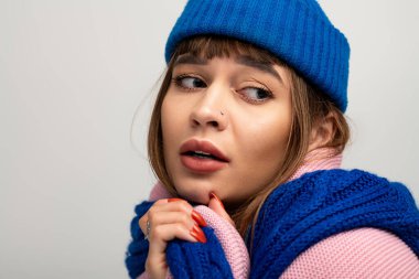 Sıcak giyimli bir kadın, zarif pozunu tarafsız bir arkaplanda sergiliyor..