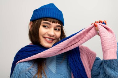 Sıcak bir gülümsemesi olan neşeli genç bir kadın, neşeli kış aksesuarlarıyla poz veriyor..