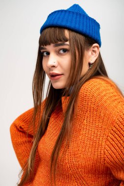 Çekici genç bayan kış boyunca rahat turuncu süveter ve mavi şapkayla rahatça poz veriyor..