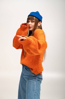 Genç bir kadın rahat turuncu bir süveter ve mavi bir bere giyer, sonbaharın özünü yakalar.