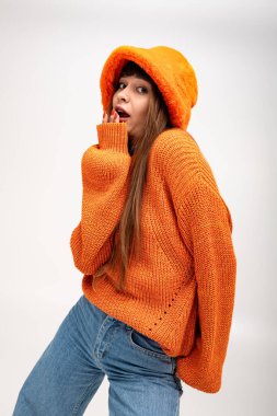 Genç bir kadın parlak turuncu bir kazak ve şapkayla poz veriyor, sıcaklığı ve tarzı var..