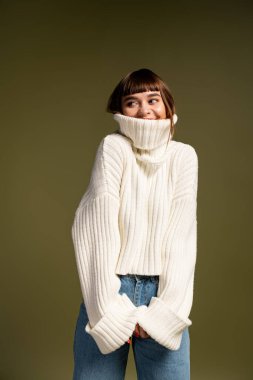 Sıcak katmanlar içindeki neşeli genç bir kadın, yumuşak bir zemine şakayla poz veriyor..