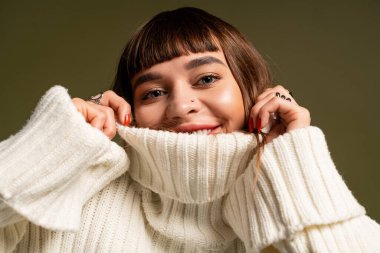 Genç bayan neşe içinde şık kıyafetlerini sergiliyor, rahat bir ortamda sıcaklığını yayıyor..