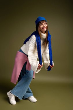 Neşeli genç bir kadın, sıcacık bir sonbahar havasıyla çevrili, sıcak sonbahar kıyafetleriyle neşeli bir şekilde poz verir..