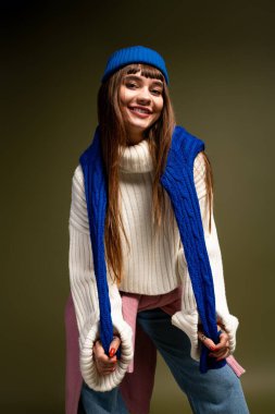 Sıcak ve şık sonbahar kıyafetleri giymiş genç bir kadın neşeli bir gülümsemeyle poz veriyor..