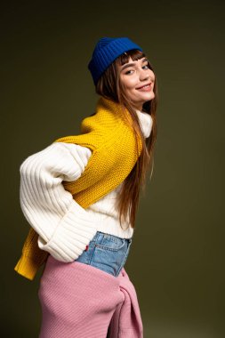 Sıcak, şık giyinmiş genç bir kadın neşeli bir duruş sergiliyor, mutluluk saçıyor..