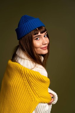 Genç bir kadın renkli kışlık giysiler içinde, sıcak ve neşe saçan pozlar veriyor..