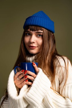 Güzel ve genç bir bayan sıcak bir anı sever mavi bir kupa tutarken.