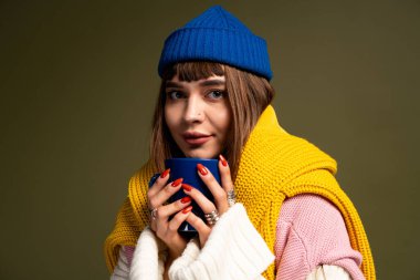 Güzel genç bir kadın sıcak bir içecek tutarken rahat kıyafetler giyer, sonbahar titreşimleri yayar..