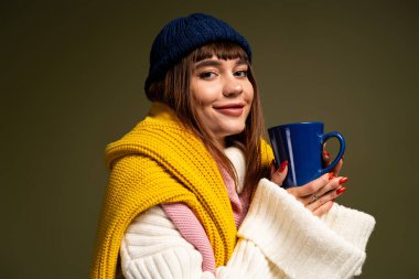 Genç bir kadın neşeyle poz veriyor. Renkli sonbahar kıyafetiyle ılık bir içecekle..