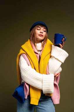 Güzel, genç bir kadın, sonbahar havasında elinde parlak bir kupayla şık bir şekilde poz veriyor..