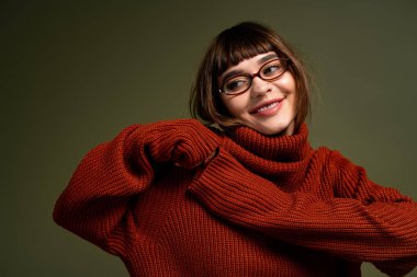 Rahat süveter giyen genç bir kadın, sessiz bir arka plana poz verirken sıcaklık ve neşe saçar..